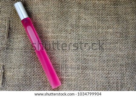 Pink oblong long thin beautiful glass matte fashionable glamorous bottle of cologne, perfume with silver cap and place for sample text on a background of brown old linen fabric