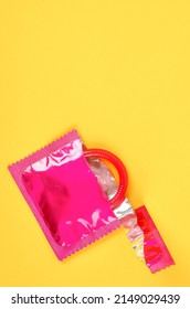 The Pink opened condom and condom in pack on a yellow background.