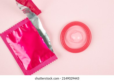 The Pink opened condom and condom in pack on a pink background.