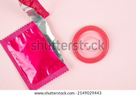 The Pink opened condom and condom in pack on a pink background.