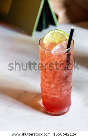 Pink Orange Alcoholic Cocktail with Lime Wedge Paper Straw on White Marble Table at Trendy Bar Copy Space