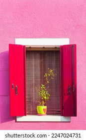 Pink painted facade of the house and window with red shutters. Colorful architecture in Burano island, Venice, Italy.