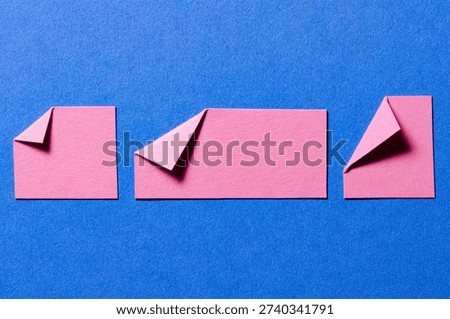 Pink paper message notes or sheets with folded edge dog-ear earmark and copy space for text on blue background, top view flat lay conceptual desk backdrop
