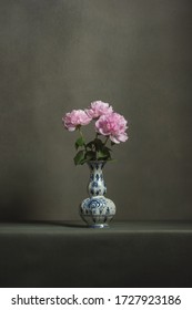 Pink peonies in a delft blue vase on a table in a grey room.