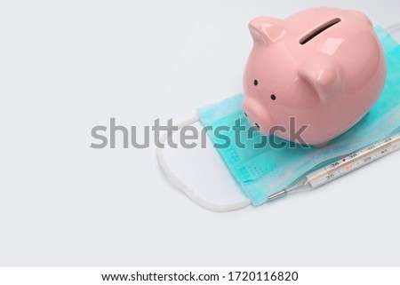 Pink pig piggy bank on a non-sterile green mask and a mercury medical thermometer