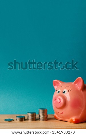 Pink piggy bank and coins in piles on a blue background. Concept - saving money or saving money. Favorable purchase. Space for text on top.