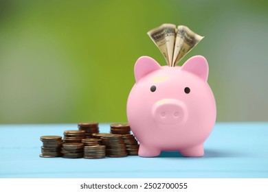 Pink piggy bank with dollar banknote and stacks of coins on light blue table against blurred background, closeup