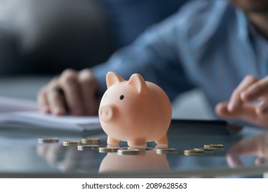 Pink piggy bank euro coins on table, close up view, man on background calculates expenses, managing finances, household bills or taxes, save money for future, take care for tomorrow, frugality concept
