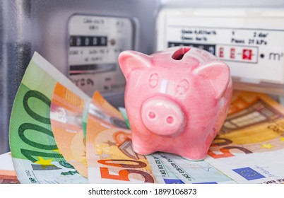 Pink piggy bank and Euro money near an electricity meter and gas meter. Utility bills, consumption of electricity and gas for heating home, energy costs, symbolic image.
