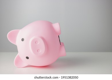 Pink Piggy Bank Falling Down On White Table Isolated On White Background. Represents The Troubled Or Failed Finance, Or Failed Deposit Money No Wealth. Money Deposit And Finance Concept.