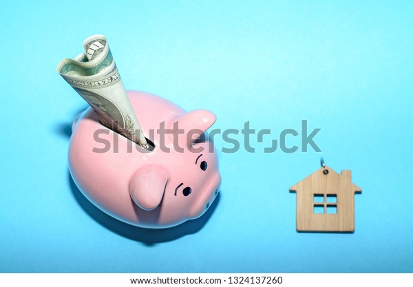 Pink piggy bank with a\
house on the table. Tinted. Concept of saving finances and real\
estate deposits