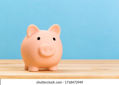 Pink Piggy Bank On Wooden Table And Blue Background. The Concept Of Storage, Accumulation. Crisis, Inflation, Financial Collapse.