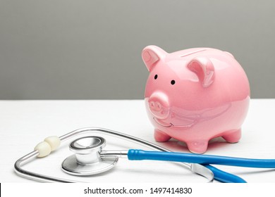 Pink piggy bank and stethoscope on a gray background. Concept of how to save on health insurance or personal insurance.
