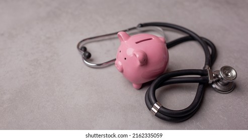 Pink Piggy Bank And Stethoscope On A Gray Background. Concept Of How To Save On Health Insurance Or Personal Insurance.