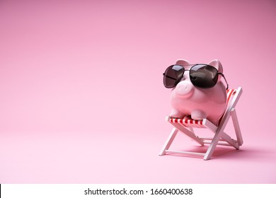 Pink Piggy Bank With Sunglasses On The Small Deck Chair On Pink Background