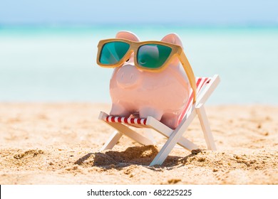 Pink Piggy Bank Wearing Wooden Sunglasses Kept On The Deck Chair At Beach