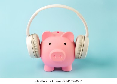 Pink piggy money bank with white wireless headphones over blue background