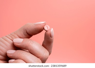 Pink pill in woman hand on pink background. Medical concept of medicine treatment, vitamins, supplements, contraceptive pills or feminine drug addiction. Close up, selective focus.