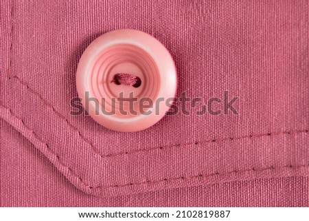 Pink plastic button sewn on pink cotton background closeup