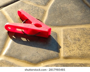 Pink plastic clothespin casting a shadow on textured stone pavement on a sunny day