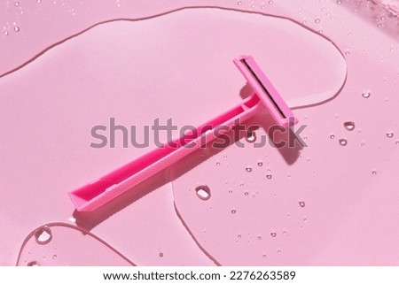 Pink plastic disposable female razor for shaving on a pink background with water. Image for your design. Hygienic products for self-care