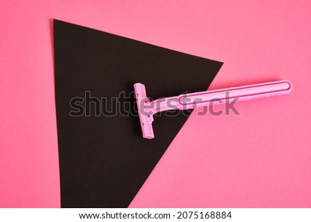 a pink plastic disposable razor and a black triangle made of paper on a pink background, an association on the theme of feminism and shaving hair from a female body