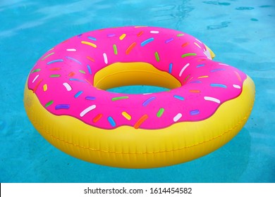 A pink plastic pool float shaped like a donut with sprinkles