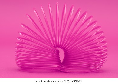 Pink plastic slinky spring bent over in an arch shape on same coloured background, close up shot