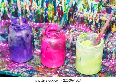 Pink, purple and yellow paint are in glass jars. Colorful background. Wooden paintbrush. Art supplies.    - Powered by Shutterstock