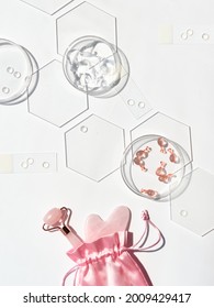 Pink Quarts Face Roller, Gua Sha Stone, Serum Capsules In Chemical Glass Dish, Hexagons. Facial Massage. Natural Cosmetics Laboratory. Off White Top View With Pink Beauty Objects, Monochromatic Look.