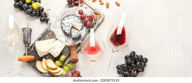 Pink and red wine served with cheeses, nuts, grapes and glasses of wine. Delicious food wine snacks assorted served on boards. Flat lay on a white background. Panorama with copy space. - Powered by Shutterstock