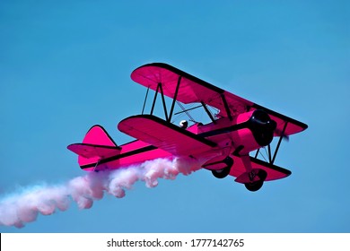 Pink retro airplane biplane isolated on sky background. Fashion vintage old airplane fly & female pilot. Pink airplane & white smoke. Airplane biplane condensation trail, smoky effect line after plane