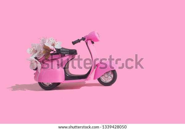 Pink retro toy bike delivering bouquet of flowers\
box on pink background. February 14 card, Valentine\'s day. Flower\
delivery. 8 March, International Happy Women\'s Day. Mother\'s\
day.