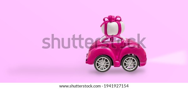 Pink retro toy car with gift box on a roof\
with on pink background.