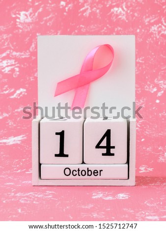 Pink ribbon of breast cancer awareness on a white wooden perpetual calendar with date 14 october. International breast cancer awareness month. Healthcare.