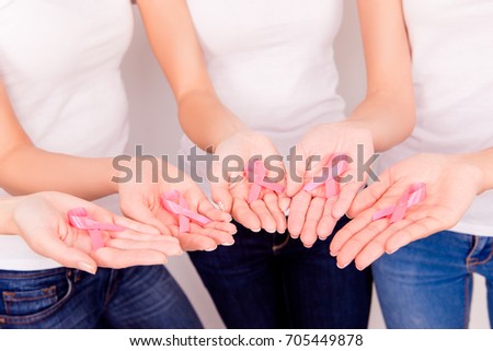 Pink ribbon for breast cancer awareness, symbolic raising awareness of women living with breast tumor illness, five female arms holding them, wearing white tshirts and jeans, closeup cropped shot