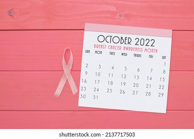 Pink Ribbon Next To Breast Cancer Awareness Month October 2022 Calendar On Wood Grain Background