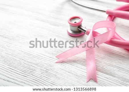 Pink ribbon and stethoscope on wooden background, space for text. Breast cancer concept