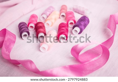 Pink ribbon and thread spools on white surface, sewing, ribbons,