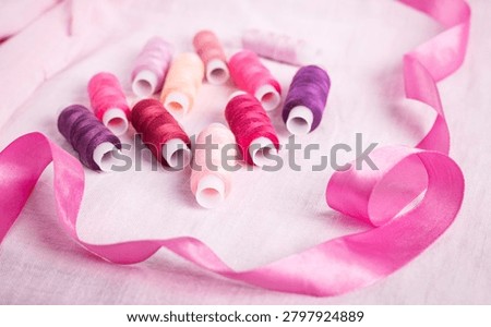 Pink ribbon and thread spools on white surface, sewing, ribbons,