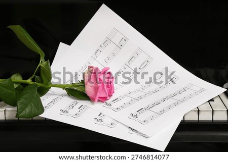 Pink rose with note sheets on piano keys, closeup. Valentine's Day celebration