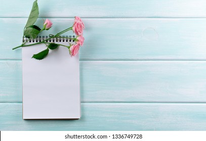 Pink roses and empty notebook with place for text on wooden background. Top view. Flat lay style.