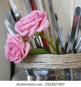 Pink roses in a glass jar with art tools - Powered by Shutterstock