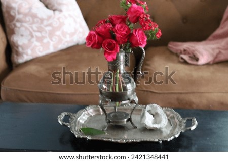 Pink roses and small red flowers on a silver tray, in a silver pitcher