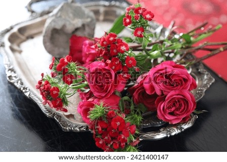 Pink roses and small red flowers on a silver tray, in a silver pitcher