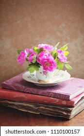 Pink roses in a teacup on a stack of old books