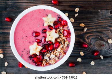 pink smoothie bowl with pomegranate, homemade granola, banana stars and chia seeds on a wooden background - Powered by Shutterstock