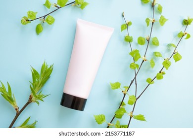 Pink Squeeze Bottle Cosmetic Tube With Screw Black Cap And Birch Branches With Young Small Leaves On Blue Background. Flat Lay, Top View.