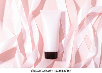 Pink Squeeze Bottle Cosmetic Tube With Screw Black Cap And Pink Gold Ribbons On Pink Background, Mockup. Daily Cream, Gel, Skin Care, Sunscreen, Moisturizer. Front View, Blank Tube