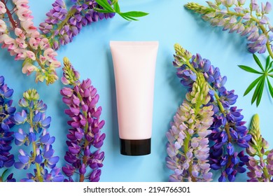 Pink Squeeze Bottle Cosmetic Tube With Screw Black Cap And Multicolored Lupine Flowers A Lot On Blue Background. Daily Cream, Gel, Skin Care, Sunscreen, Moisturizer. Front View, Blank Tube